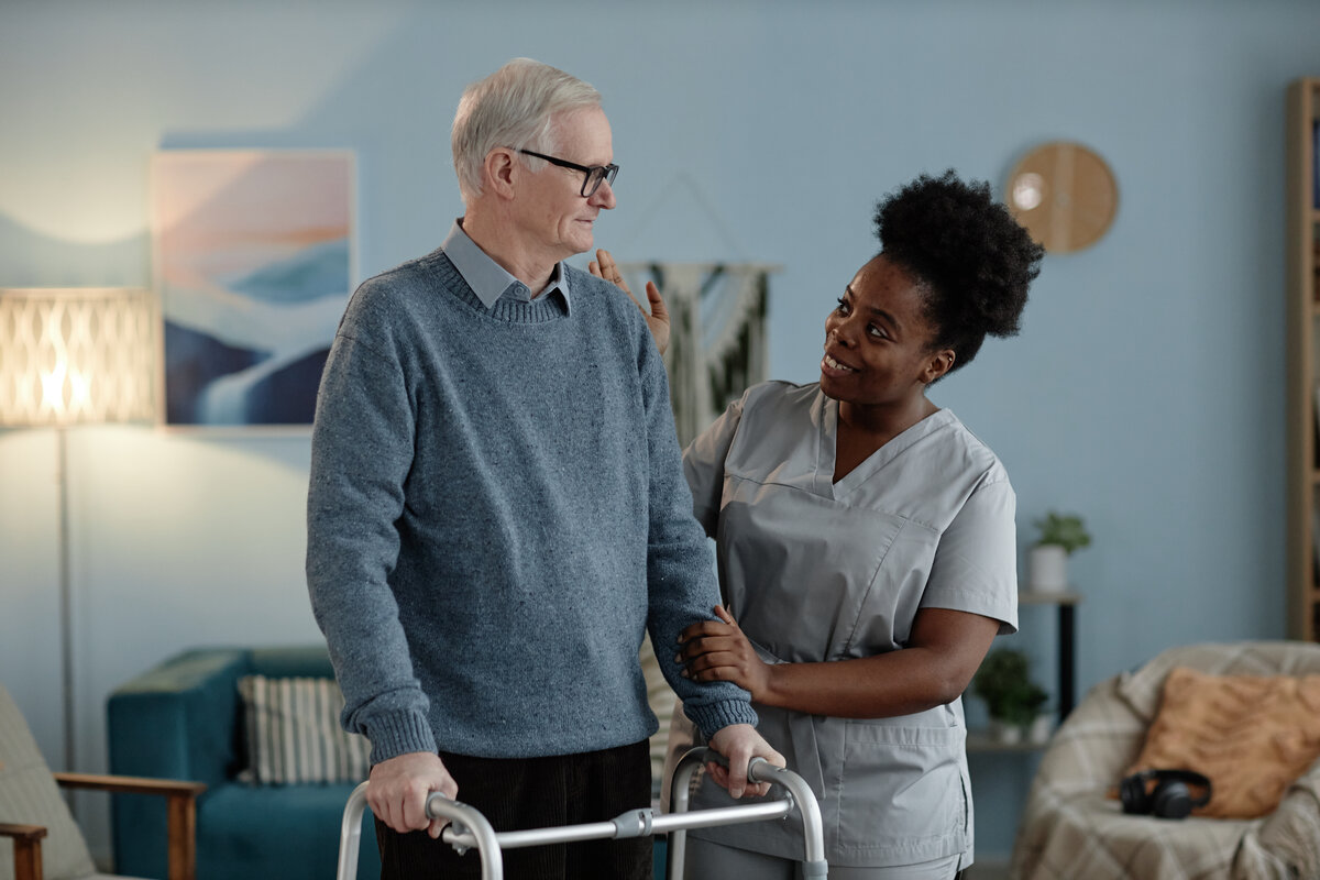 Professional caregiver providing compassionate home care support to elderly gentleman with walker, demonstrating Clover Support Group's person-centered care approach