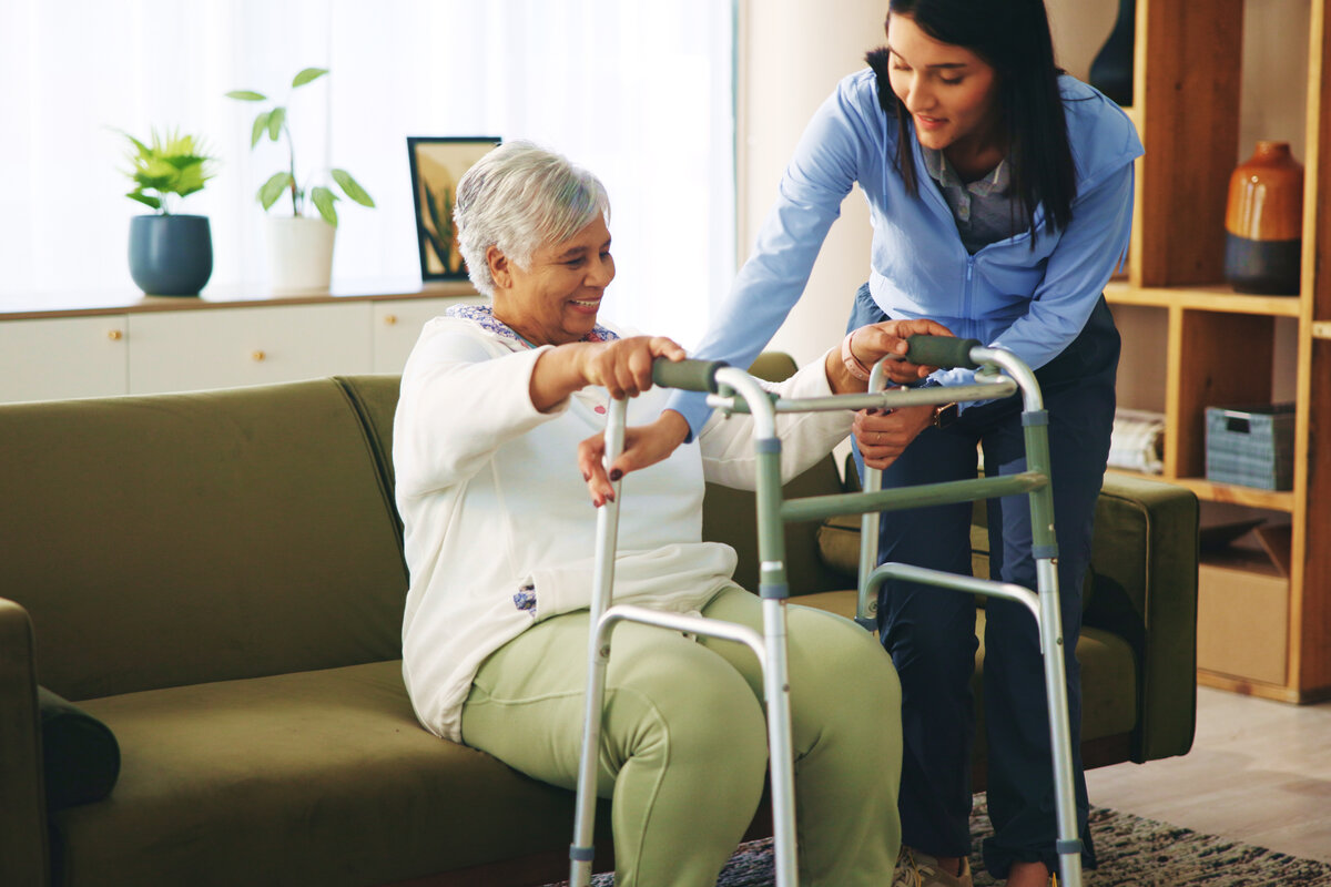 Caregiver helping elderly woman with walker in comfortable home setting