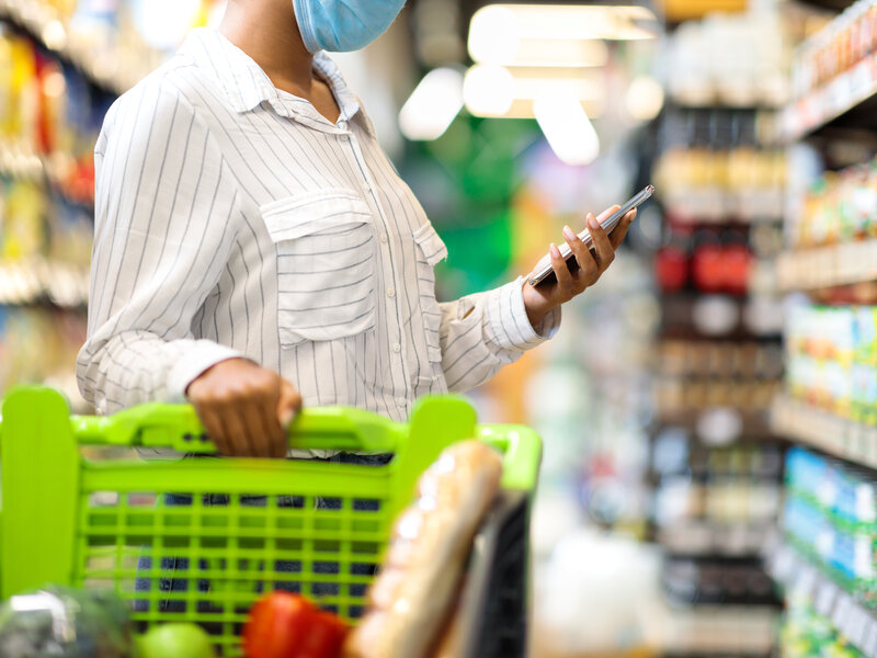 Person using smartphone while grocery shopping, demonstrating independence and technology support for daily living tasks